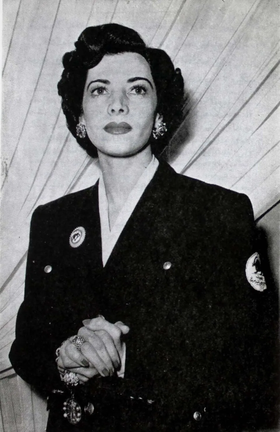 Shams Pahlavi de uniforme escuro da Sociedade do Leão e Sol Vermelhos do Irã, com o emblema num distintivo costurado na manga esquerda e uma insígnia no peito