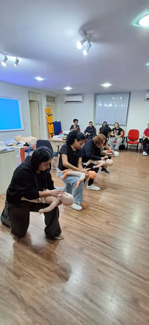 Alunos praticando a manobra de desengasgo em manequins de bebê durante a aula