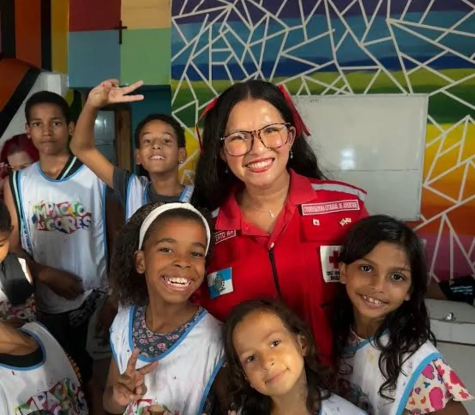 Coordenadora de Juventude da filial sorrindo com crianças do projeto Impacto das Cores, de camiseta do projeto, diante de um muro pintado