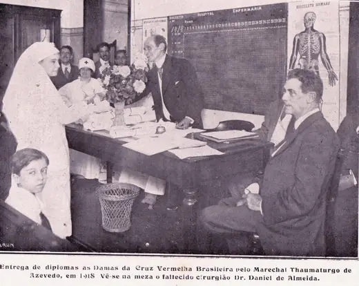 Diploma ceremony, with nurses standing before a table and men seated