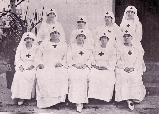 Nine nurses in white uniforms, seated in three rows