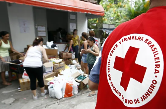 Voluntário de costas, com colete da Cruz Vermelha Brasileira, Filial do Estado do Rio de Janeiro, diante de uma distribuição de donativos
