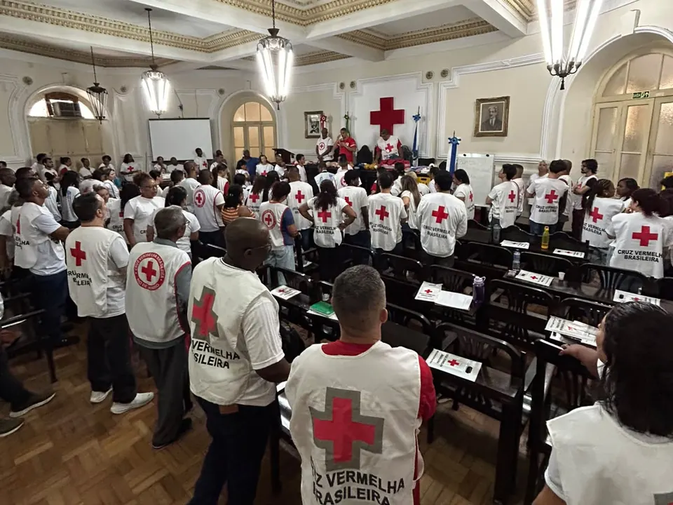 Voluntários de camiseta da Cruz Vermelha Brasileira, vistos de costas, na formação do CBFI no salão nobre da sede