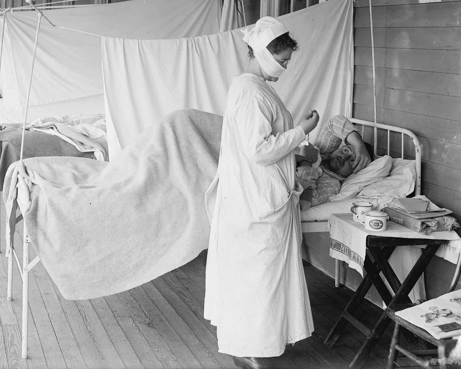 Enfermeira de máscara cuida de um paciente em uma enfermaria de gripe espanhola, em 1918, nos Estados Unidos