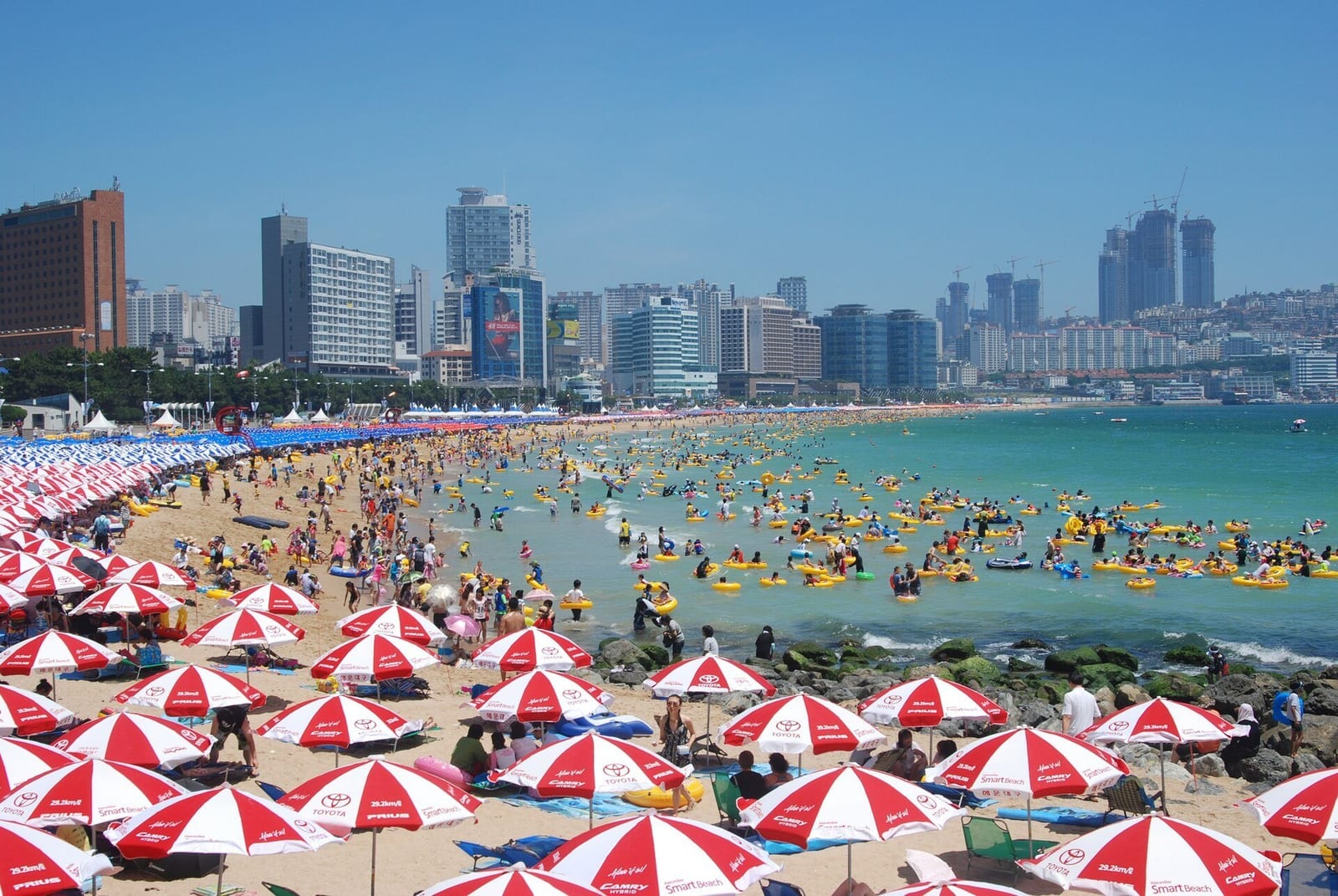 Praia cheia de banhistas sob guarda-sóis listrados, em um dia de sol forte