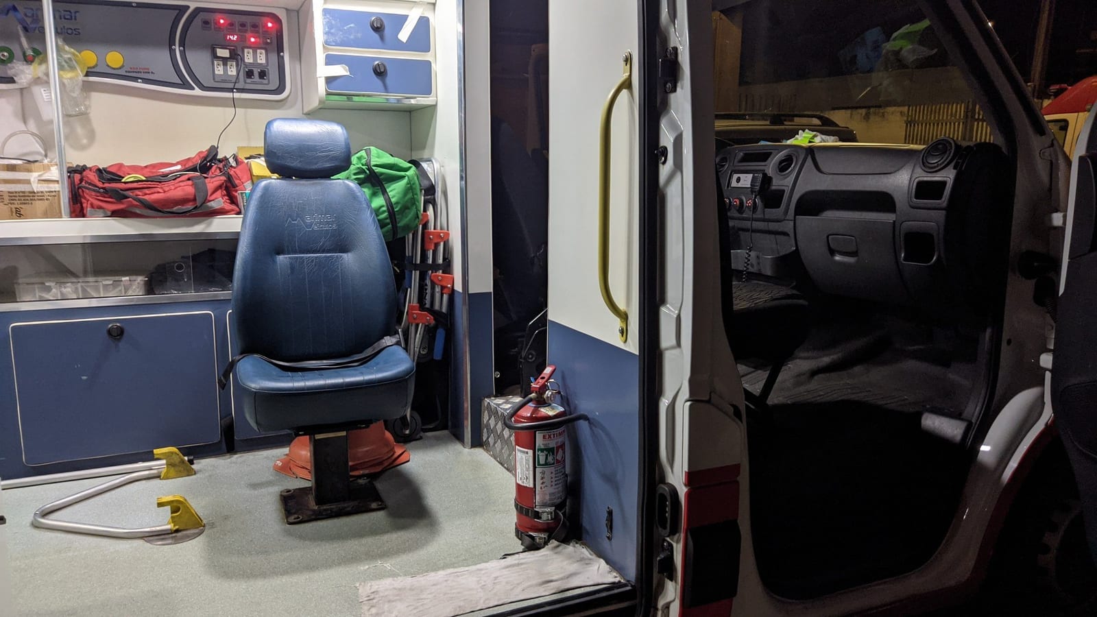 Interior de uma ambulância do SAMU, com a porta lateral aberta, cadeira e equipamentos presos à parede