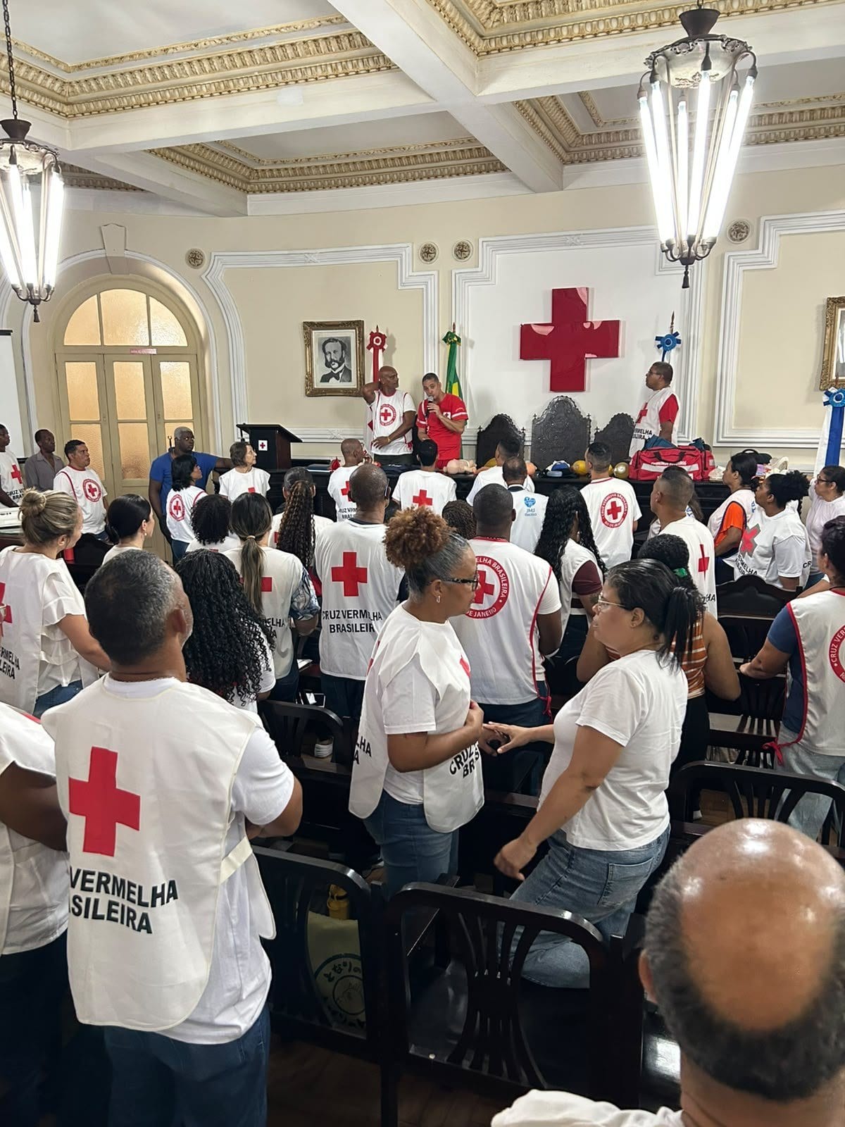 Voluntários de colete da Cruz Vermelha, de costas, em um salão de treinamento do Palácio da Cruz Vermelha